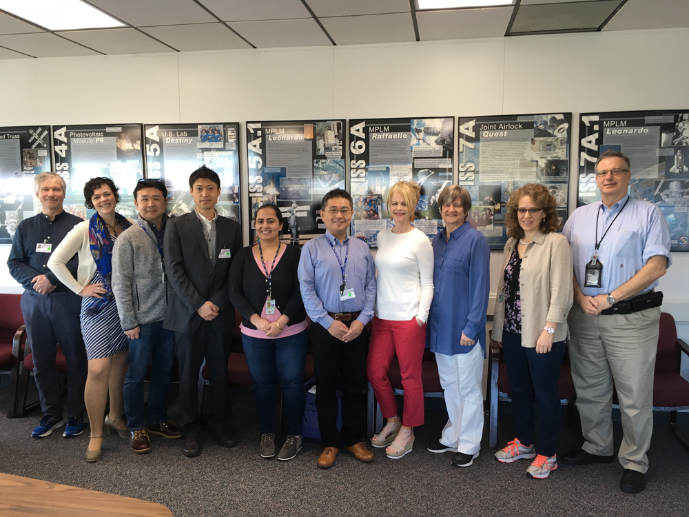 A group of men and women pose in front of posters about the International Space Station.